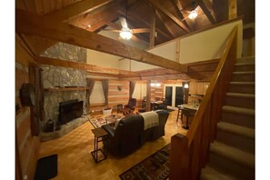 A spacious loft-style living area with a stone fireplace, wooden beams, and a staircase.