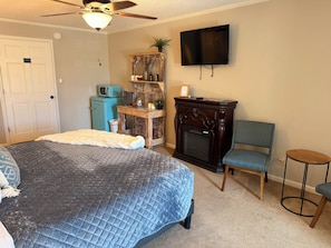 A bedroom with a large bed, a small desk, a television, and a fireplace.