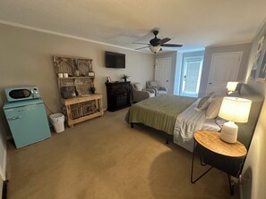 Een slaapkamer met een bed, bureau, stoel, magnetron, televisie en plafondventilator.