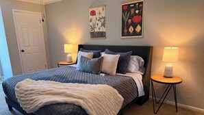 Una cama bien hecha con un cabecero acolchado, dos lámparas de noche y un cuadro floral sobre la cama.