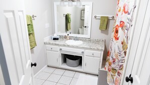 Un baño con lavamanos blanco, un espejo y una cortina de ducha estampada con motivos florales.