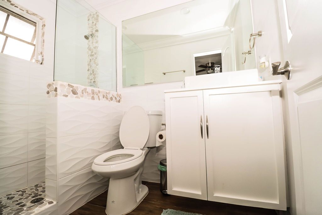 Une salle de bain avec des toilettes blanches, un miroir, un lavabo et un meuble de rangement.
