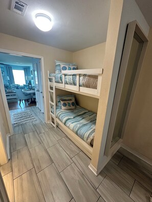 A room with a bunk bed, a dining area with a table and chairs, and a hallway leading to another room.