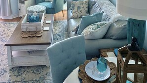 A living room with a view of a snowy landscape through a large window, featuring a blue sofa, matching lamps, and nautical-themed decor. - Amazing Unobstructed Beach Views! 🏖️Beautifully equipped with nice furnishings! (Gulf Shores)