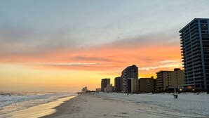 A beach with a sunset, buildings in the background, and a sandy path. - Amazing Unobstructed Beach Views! 🏖️Beautifully equipped with nice furnishings! (Gulf Shores)