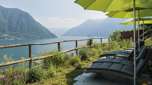 A lakeside view with a wooden railing, lounge chairs, and a large umbrella. - Ca' de Sass near Argegno Lake Como (Colonno)
