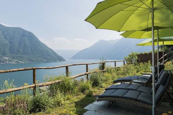 A lakeside view with a wooden railing, lounge chairs, and a large umbrella.