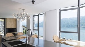 A modern kitchen with a large island, a dining area with wicker chairs, and a view of a lake and mountains. - Ca' de Sass near Argegno Lake Como (Colonno)