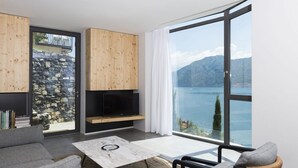 A modern living room with a stone wall, wooden cabinets, a flat-screen TV, and a large window with a lake view. - Ca' de Sass near Argegno Lake Como (Colonno)