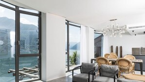 A modern interior with large windows, a dining area with wicker furniture, and a view of a body of water. - Ca' de Sass near Argegno Lake Como (Colonno)