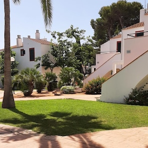 A residential area with white buildings, a paved walkway, and green landscaping.