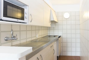 Una cocina con microondas integrado, encimera de acero inoxidable y paredes con azulejos blancos.
