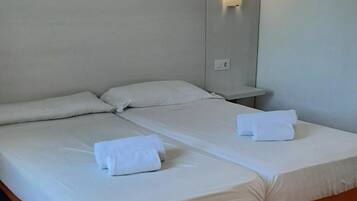 Uma cama de casal com lençóis brancos, mesa de cabeceira com abajur e luminária na parede.