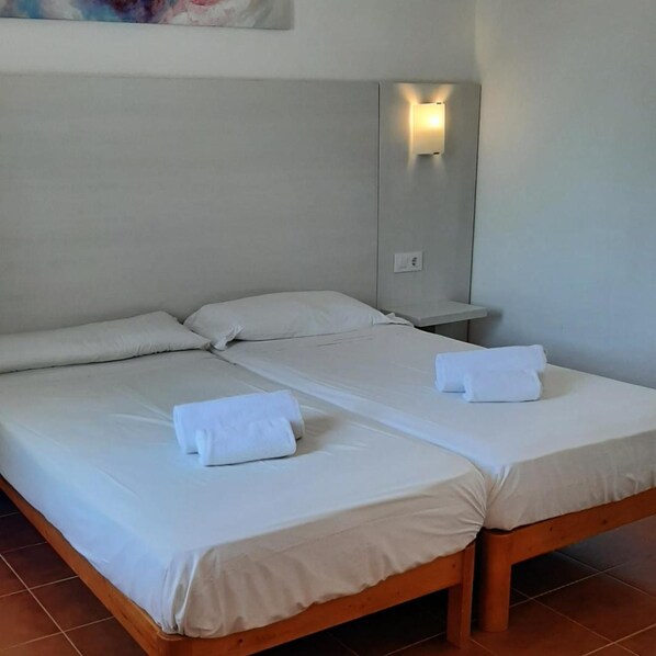 A double bed with white linens, a nightstand with a lamp, and a wall-mounted light fixture.