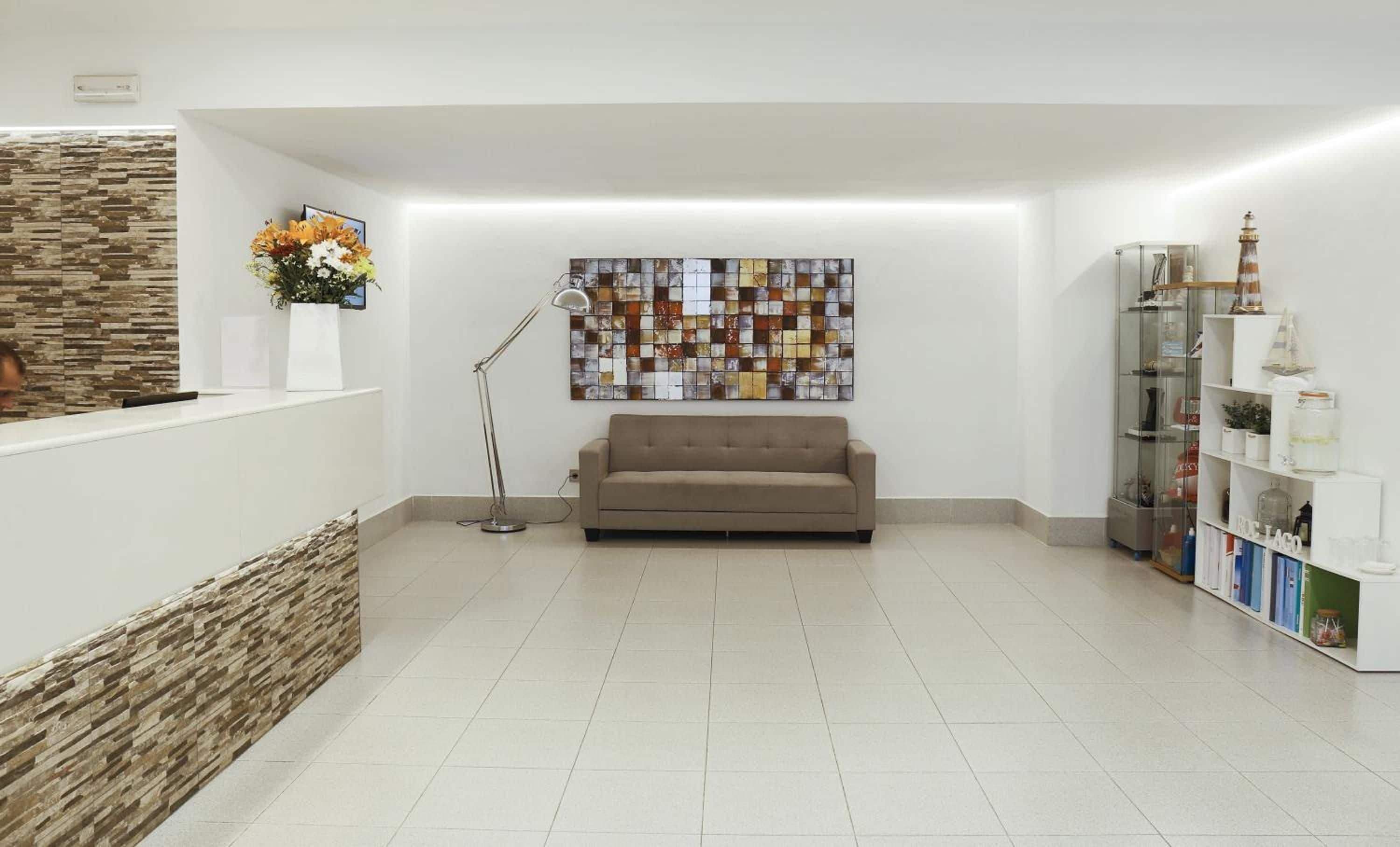 Uma área de recepção com sofá, balcão, obra de arte na parede, luminária de chão e vitrine de vidro.