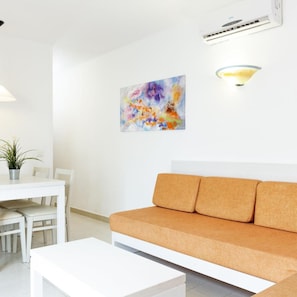 Una sala de estar moderna con un sofá blanco, una mesa de comedor con sillas y un cuadro abstracto de colores en la pared.