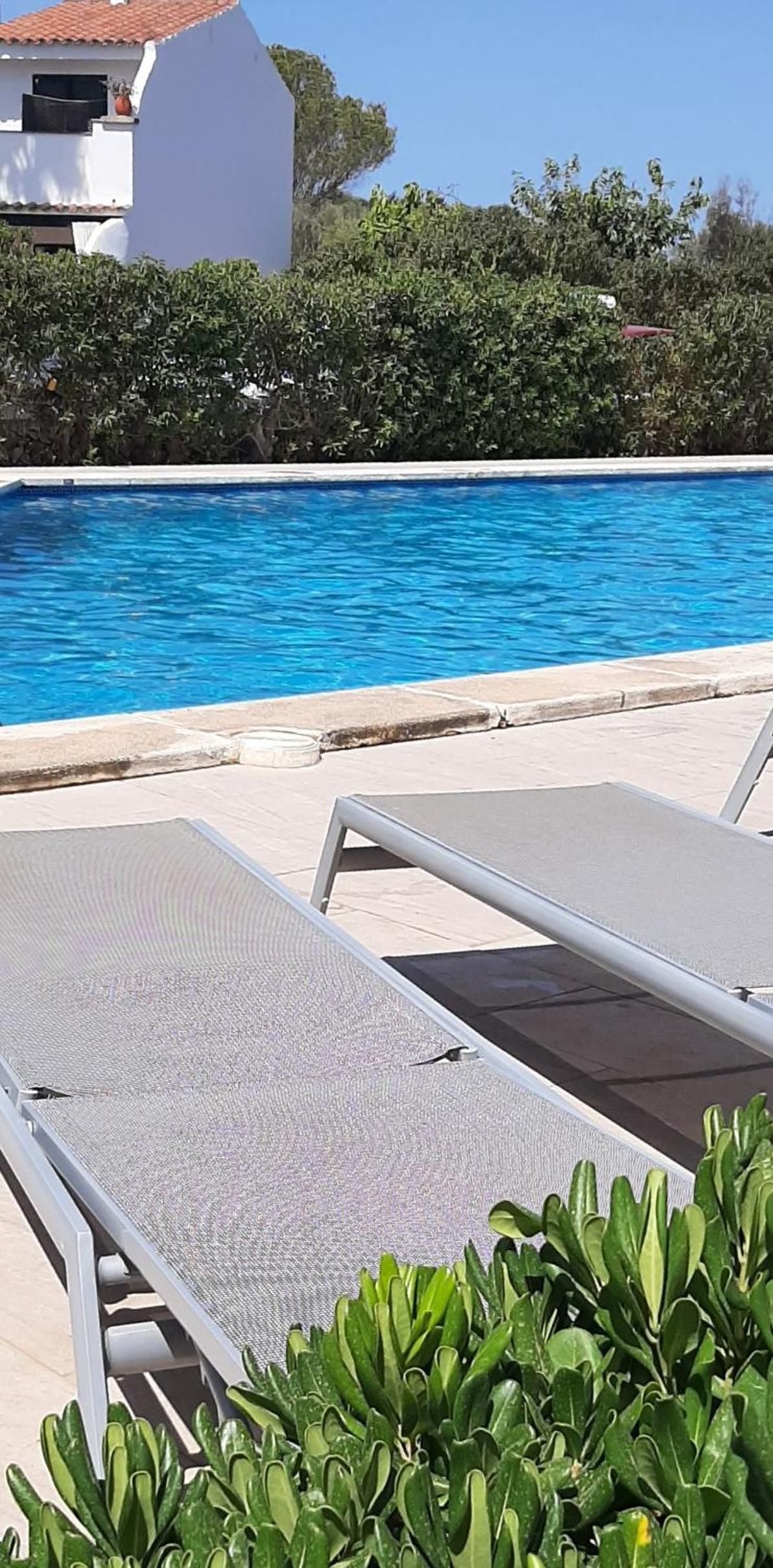 Área ao lado da piscina com espreguiçadeiras e uma piscina azul cristalina.
