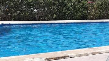 Área ao lado da piscina com espreguiçadeiras e uma piscina azul cristalina.