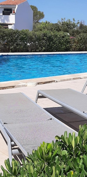 A poolside area with lounge chairs and a clear blue pool.
