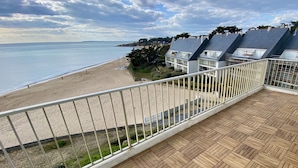 Une terrasse en bois dotée d’une rambarde, qui offre une vue sur une plage et un quartier résidentiel.