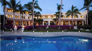 A resort with a large pool, palm trees, and a well-lit building with multiple balconies. - Beautiful luxuries affordable, quiet ocean view one bedroom home away from away (San Jose del Cabo)