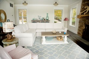 A living room with a white sectional sofa, a wooden coffee table, and a stone fireplace.