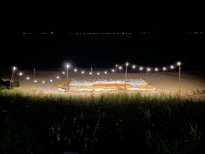 A beachside setup with a table covered with a white cloth, surrounded by string lights and various items.