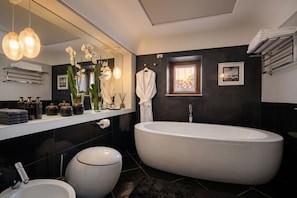 A modern bathroom with a large bathtub, a separate toilet, a vanity with a mirror, and a towel rack.