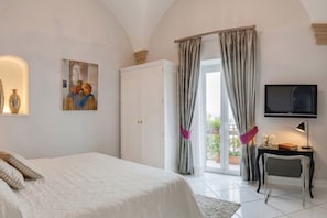 A bedroom with a bed, a television, a desk with a chair, a window with curtains, and a painting on the wall.