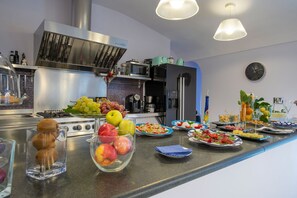Una cocina moderna con electrodomésticos de acero inoxidable, una variedad de frutas y verduras sobre la encimera y un reloj en la pared.