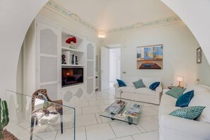 Een woonkamer met een witte bank, een glazen salontafel en een boekenkast.
