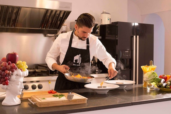 A chef cooking in a modern kitchen with stainless steel appliances and a marble countertop.