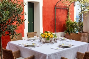 A table set for dining with a bowl of lemons and glasses, wicker chairs, and a red wall in the background.