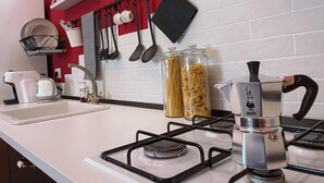 A modern kitchen with a gas stove, a coffee maker, and various utensils hanging on a rack. - WellHome   "Barbera" Apartment (ASTI)