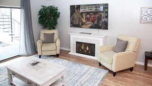 Una sala de estar con chimenea, dos sillones, una mesa de centro y un televisor de pantalla plana grande montado sobre la chimenea.