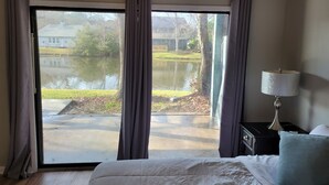 Un dormitorio con una ventana grande, una cama, una mesita de noche y una lámpara.