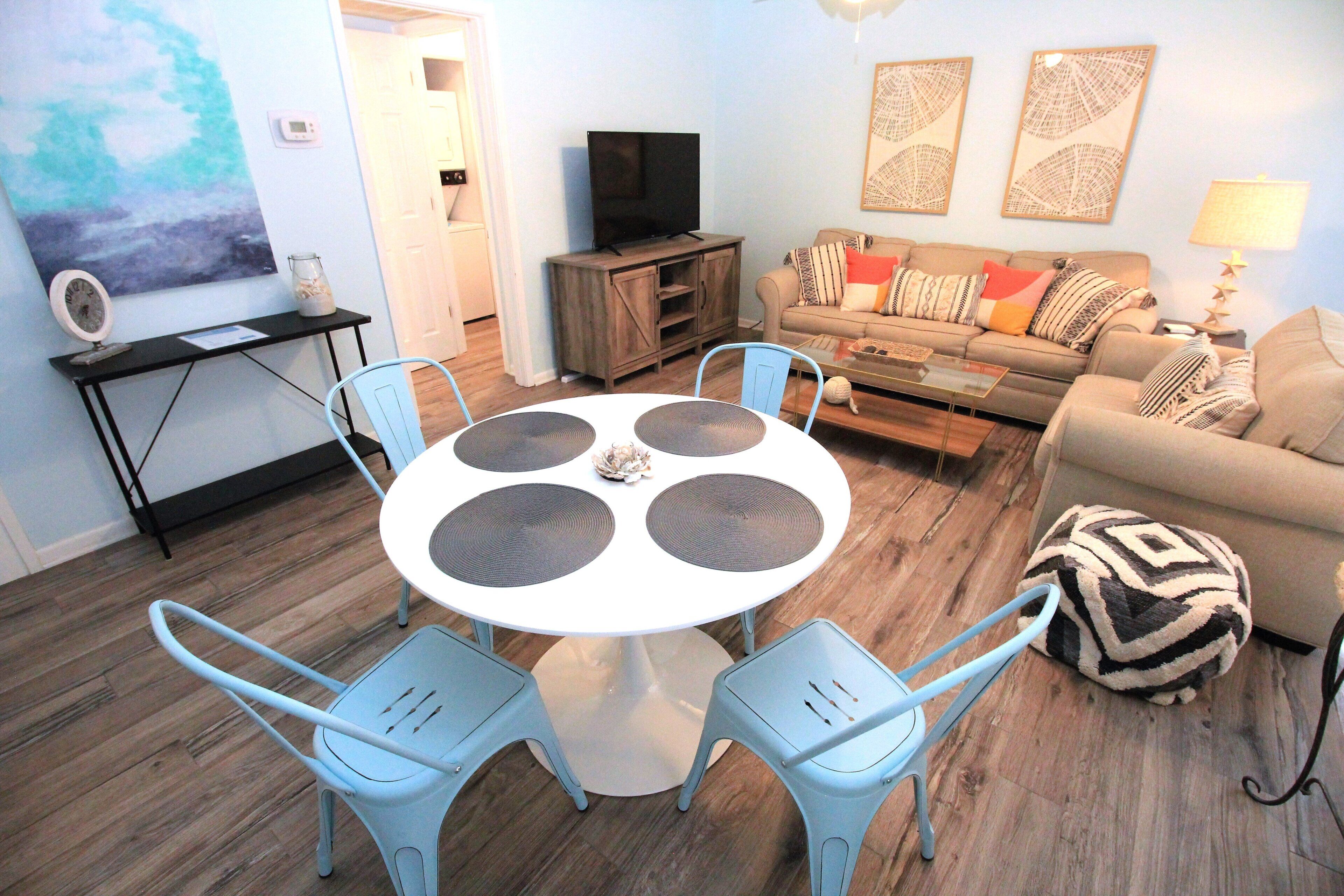 A living room with a round table, four chairs, a sofa, a television, and artwork on the wall.