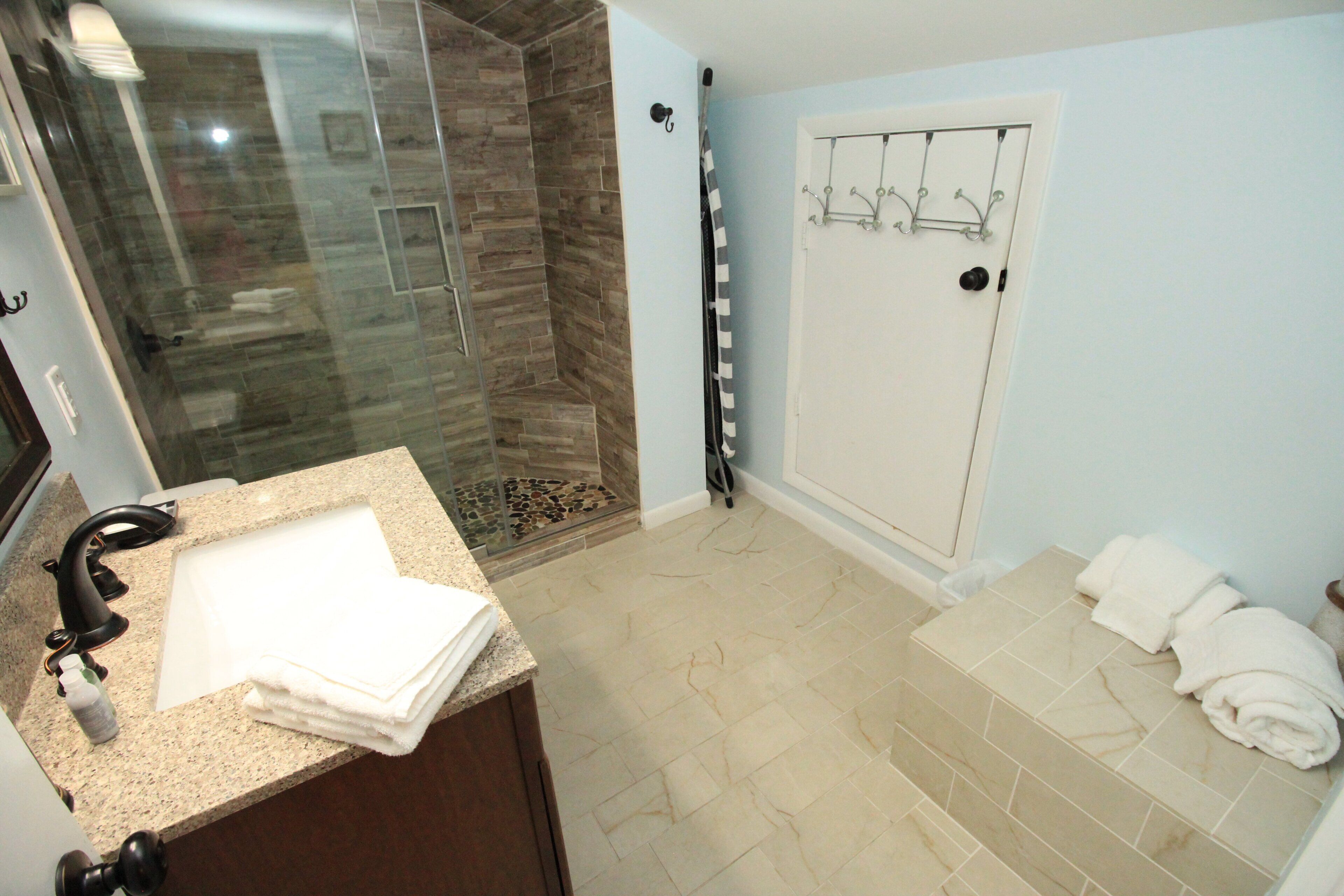 Une salle de bain avec une douche à parois de verre, un lavabo avec une pile de serviettes et un porte-serviettes mural.