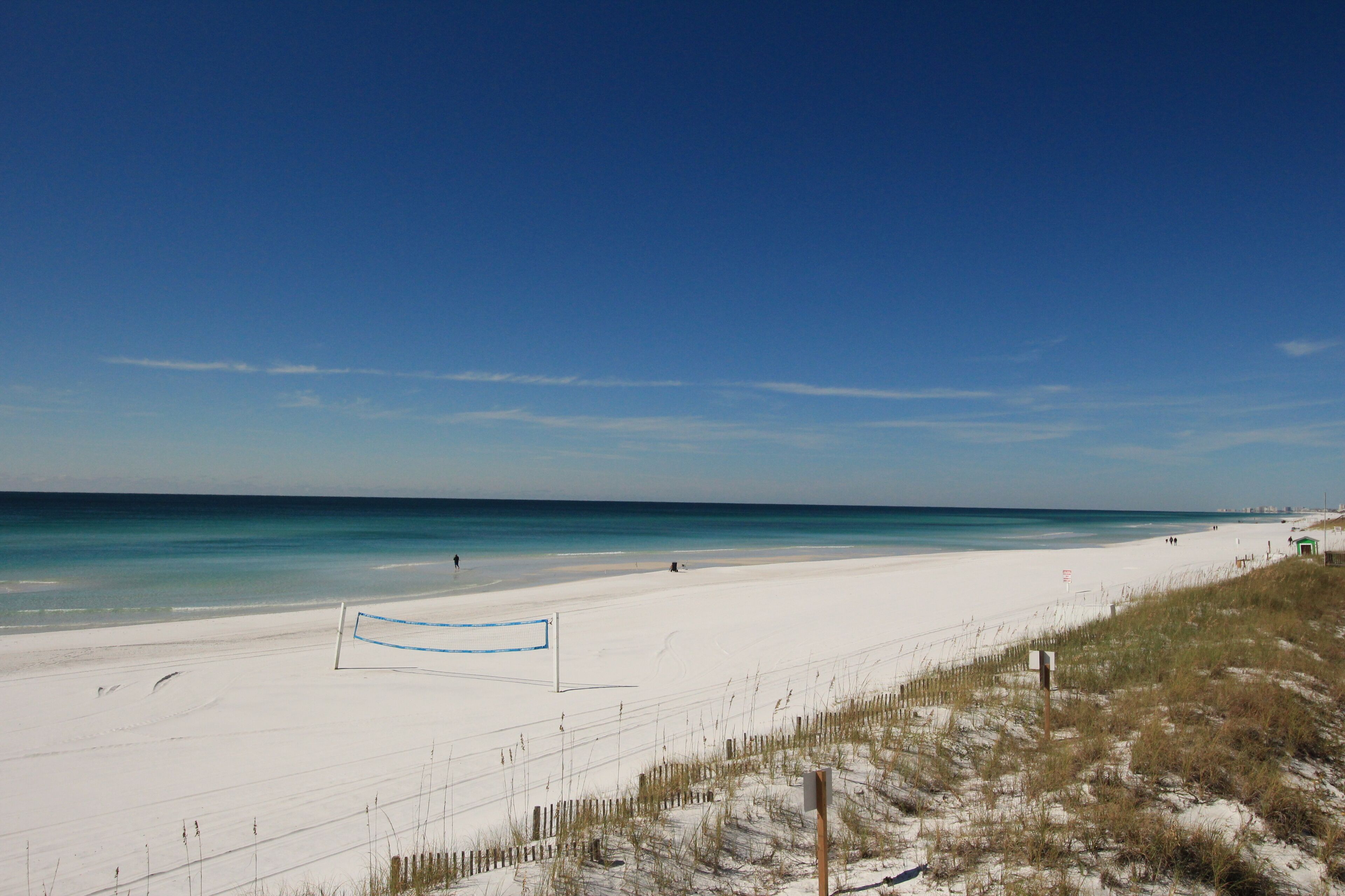 A beach with a volleyball net, sandy dunes, and a clear blue sky.