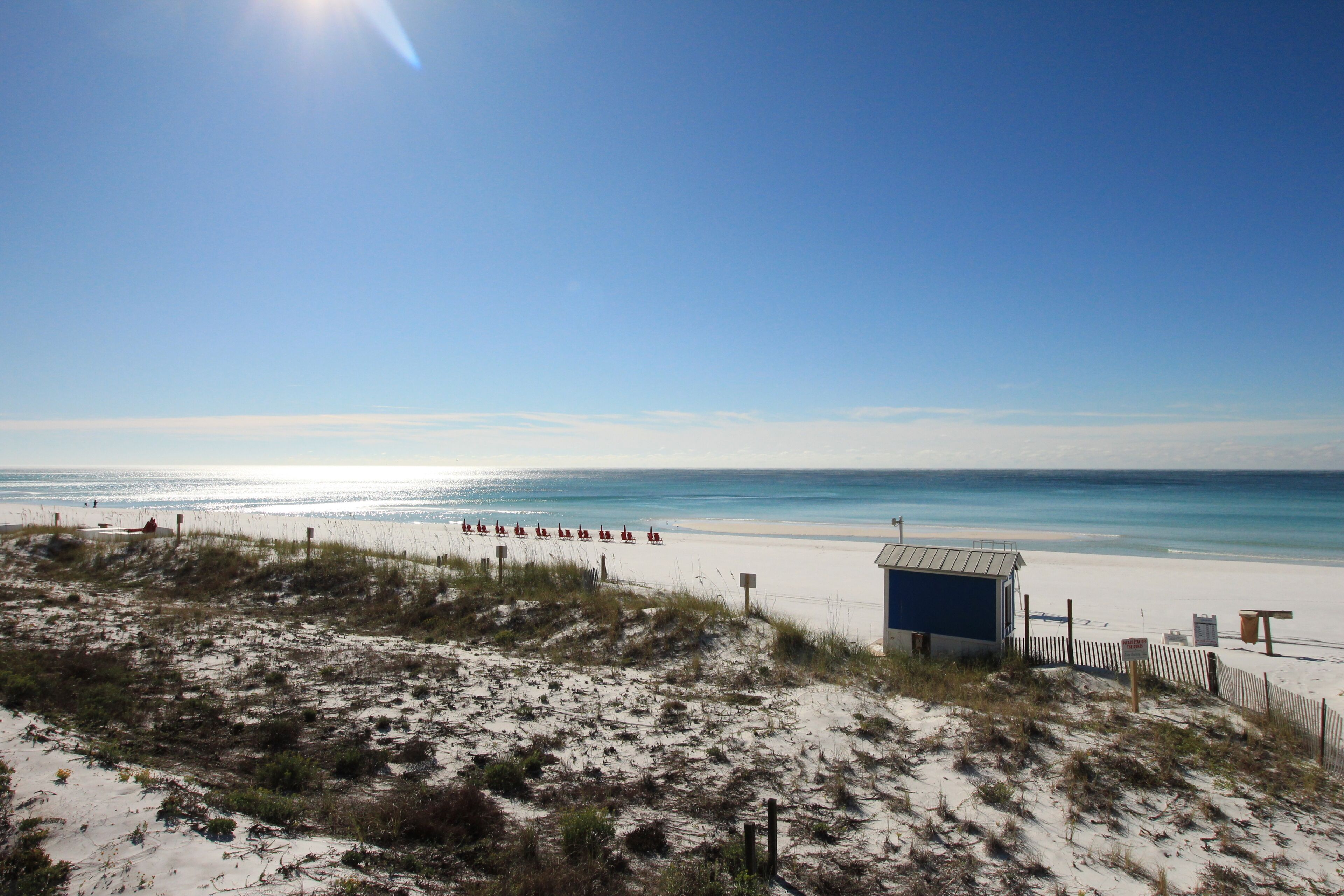 A beach with a small blue building, sandy dunes, and the ocean.