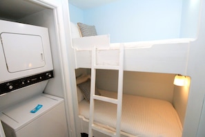 Una cama litera con escalera, un pequeño armario blanco con un electrodoméstico Kenmore y una sola almohada en la cama superior.
