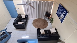 A room with two black leather sofas, a woven round table, a ceiling fan, and a TV on a stand. - Emthree Seaside Apartments (North Ward)
