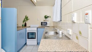 A compact kitchen with blue cabinets, a white refrigerator, a microwave, and a sink. - Emthree Seaside Apartments (North Ward)