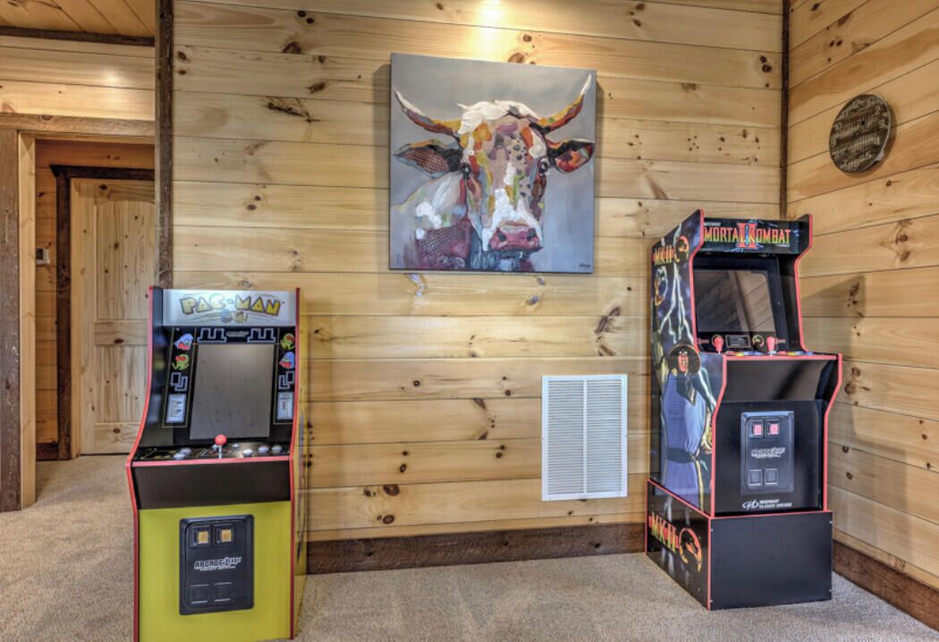Una habitación con paredes de madera, una máquina arcade de Pac-Man, una máquina arcade de Mortal Kombat y un cuadro de un toro.