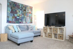 Uma sala de estar com um sofá azul claro, uma grande pintura abstrata, uma televisão de tela plana e um móvel de armazenamento com vários compartimentos.