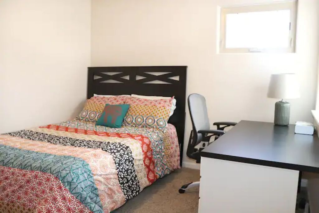 A bedroom with a bed, a desk, a chair, and a lamp.