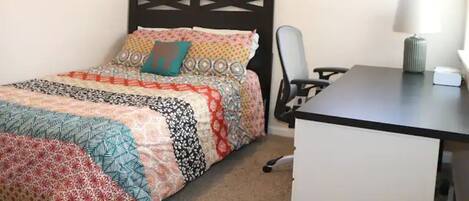 A bedroom with a bed, a desk, a chair, and a lamp.