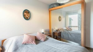 A neatly made bed with patterned bedding, a bedside table with a lamp, and a large mirror reflecting the room.