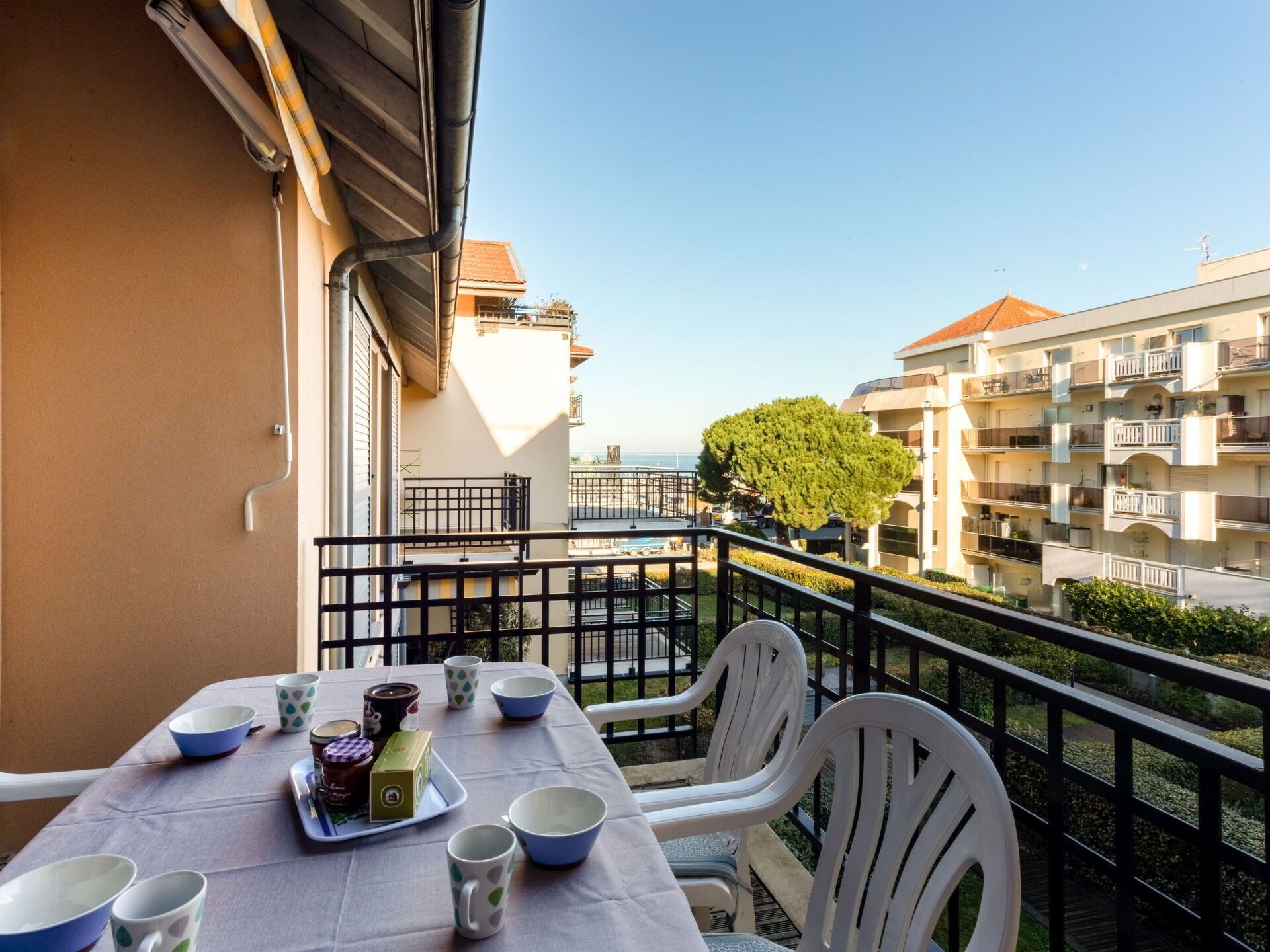 Un balcón con mesa dispuesta para comer, sillas y vistas al mar y edificios.
