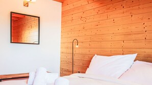 Un lit bien fait, avec du linge de lit et des serviettes blanches, une tête de lit en bois, un miroir fixé au mur et une lampe sur pied.